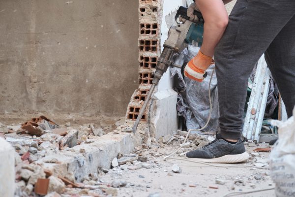 Unrecognizable worker using a jackhammer to drill into wall. Construction site.